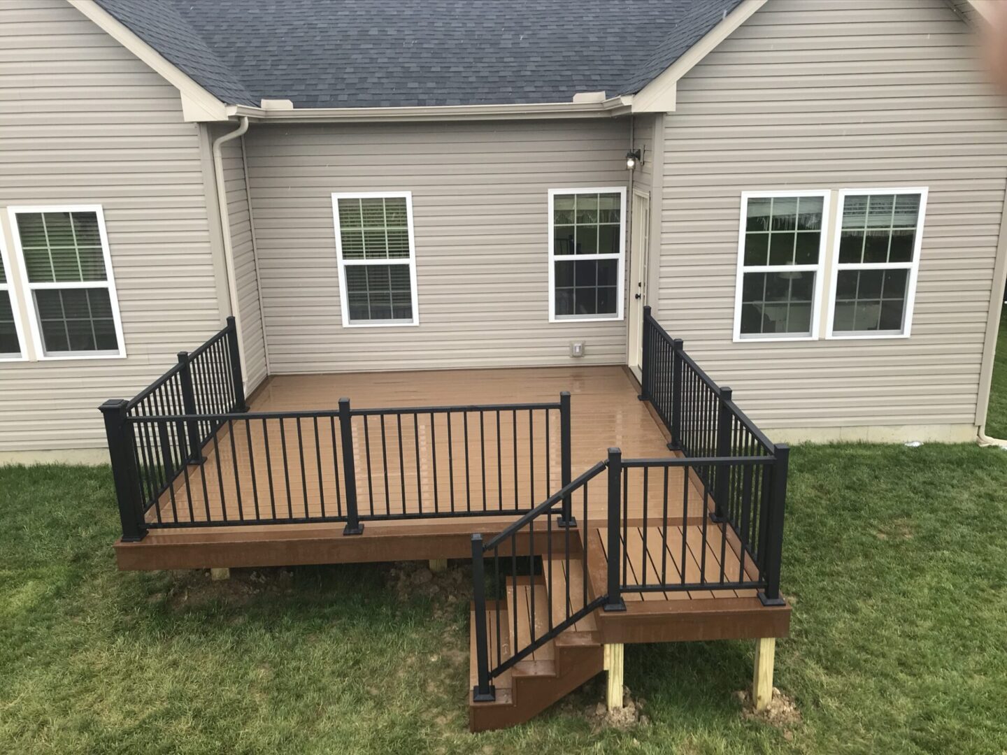 A deck with stairs and railing in the middle of a yard.