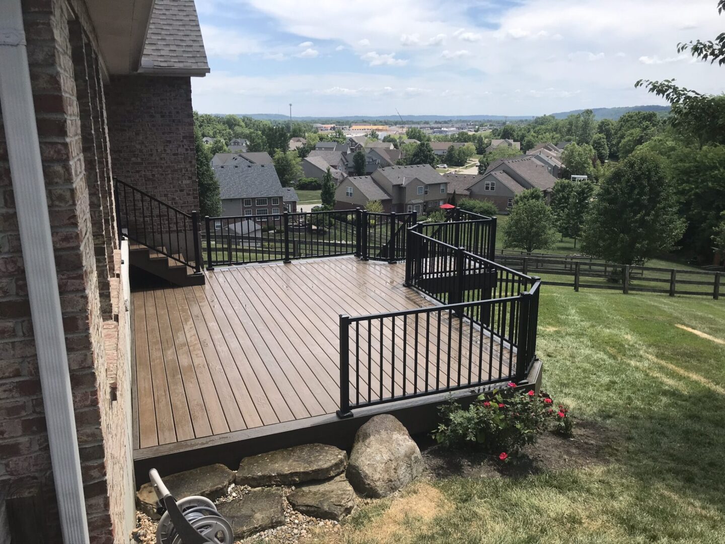 A large deck with stairs and railing in the middle of a yard.
